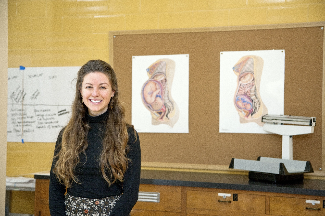 A woman is standing in front of a poster of a woman's uterus.